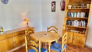 Een eetgedeelte met een ronde tafel en vier stoelen, een boekenkast en een brandblusser aan de muur.