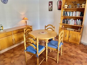 Een eetgedeelte met een ronde tafel en vier stoelen, een boekenkast en een brandblusser aan de muur.