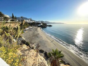Une plage côtière avec un ciel dégagé, une côte rocheuse et des bâtiments en arrière-plan.