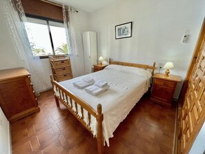 Une chambre à coucher avec un lit en bois, deux tables de chevet avec des lampes, une armoire et une fenêtre avec des rideaux.