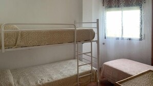 Een slaapkamer met een stapelbed, een tafeltje en een raam met gordijnen.