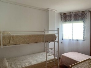Een slaapkamer met een stapelbed, een tafeltje en een raam met gordijnen.