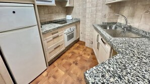 Een kleine keuken met een magnetron, oven, spoelbak en granieten aanrecht.