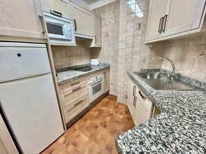 Een kleine keuken met een magnetron, oven, spoelbak en granieten aanrecht.