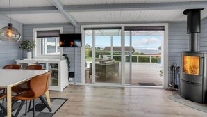 Una cocina moderna con un televisor grande, un comedor con sillas, una terraza de madera y un estufa de leña.
