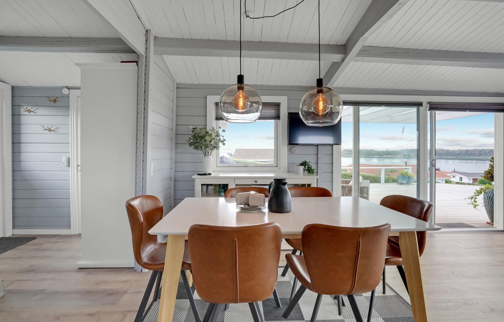A modern dining area with a white table, brown leather chairs, and pendant lights.