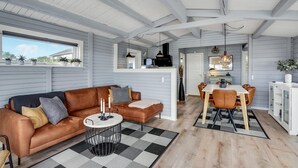 Una sala de estar moderna con un sofá de cuero, un comedor con una mesa y sillas de madera, y una cocina al fondo.
