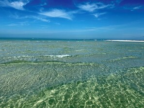 A clear view of a beach with shallow water and distant boats.