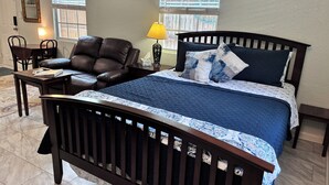 Une chambre avec un lit en bois foncé, une couette bleue, des coussins à motifs, une table de chevet, une lampe et un panneau décoratif au mur.