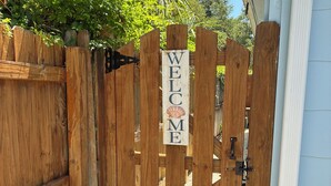 Une porte en bois avec une pancarte indiquant « BIENVENUE », un loquet métallique et une petite marche menant à une porte.