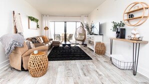 Una sala de estar moderna con sofá, una mesa de centro y una silla colgante. Hay un televisor y una cafetera sobre una encimera.