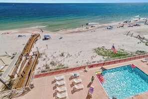 Una playa con un paseo marítimo de madera, una piscina y sillas de playa.