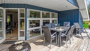 Una veranda esterna con tavolo e sedie, un barbecue e vista sull'interno tramite ampie porte in vetro.