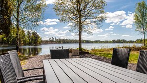 A wooden table with four wicker chairs, set on a gravel area with a view of a lake and forest. - Nice home in Hallaryd with kitchen (Hallaryd)
