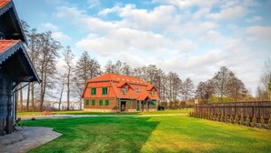 Une maison traditionnelle à deux étages, avec un toit rouge et des volets verts, entourée d’une pelouse bien entretenue et d’une clôture en bois.