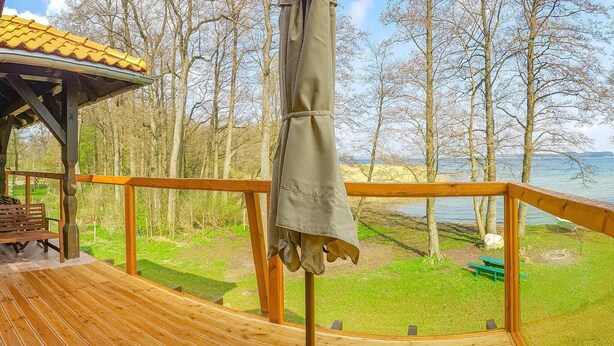Une terrasse en bois avec un banc et un espace abrité, offrant une vue sur un lac et une forêt.