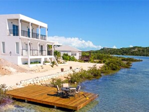 A modern two-story house with a wooden deck extending into a lake, surrounded by greenery and a clear sky. - Flamingo Lake Villas | Turks and Caicos Islands (Providenciales)