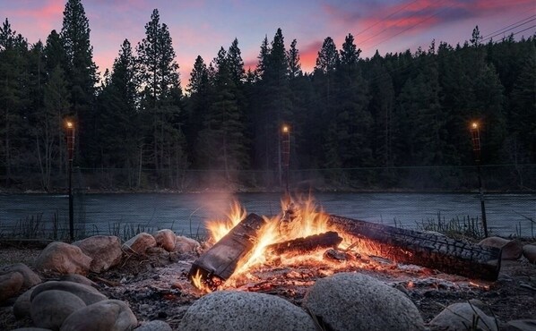 A campfire surrounded by rocks and a forested area with a lake in the background.