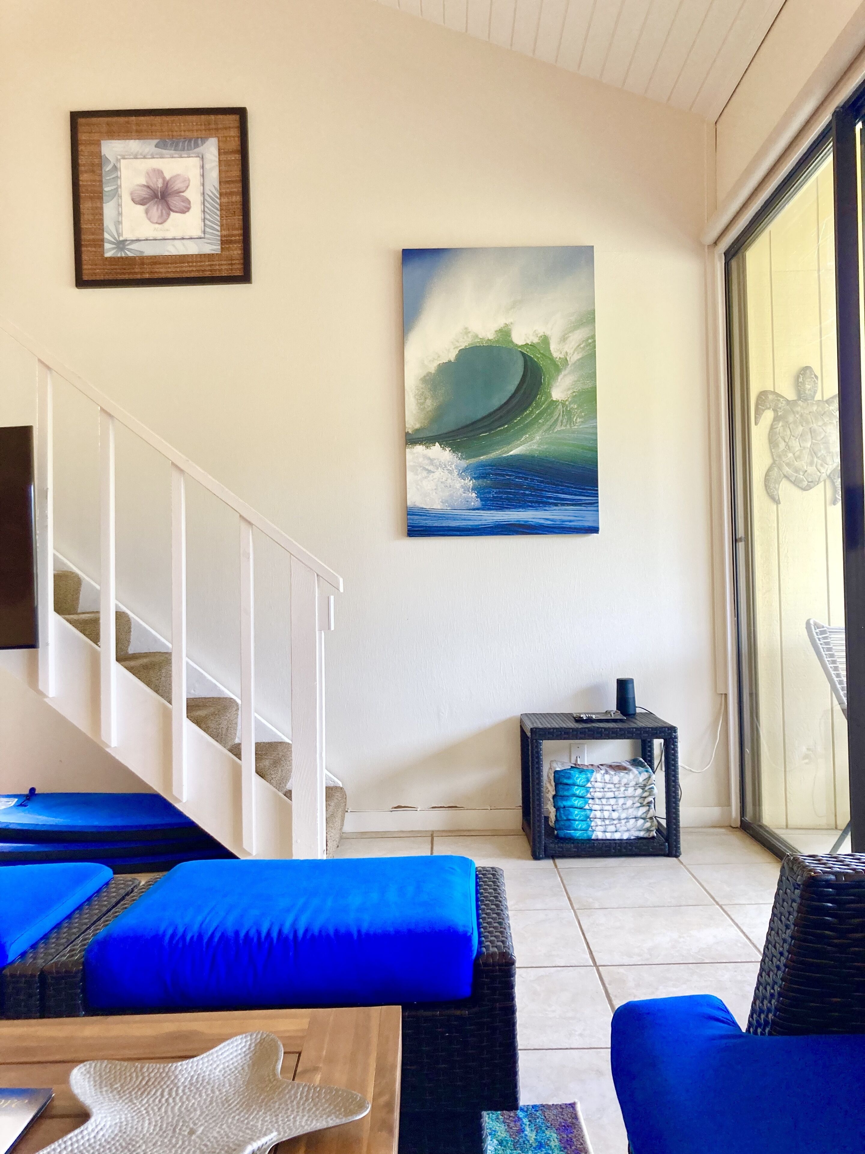 Una sala de estar con un sofá, una mesa de centro, un cuadro enmarcado, una pintura de una ola y una escalera.