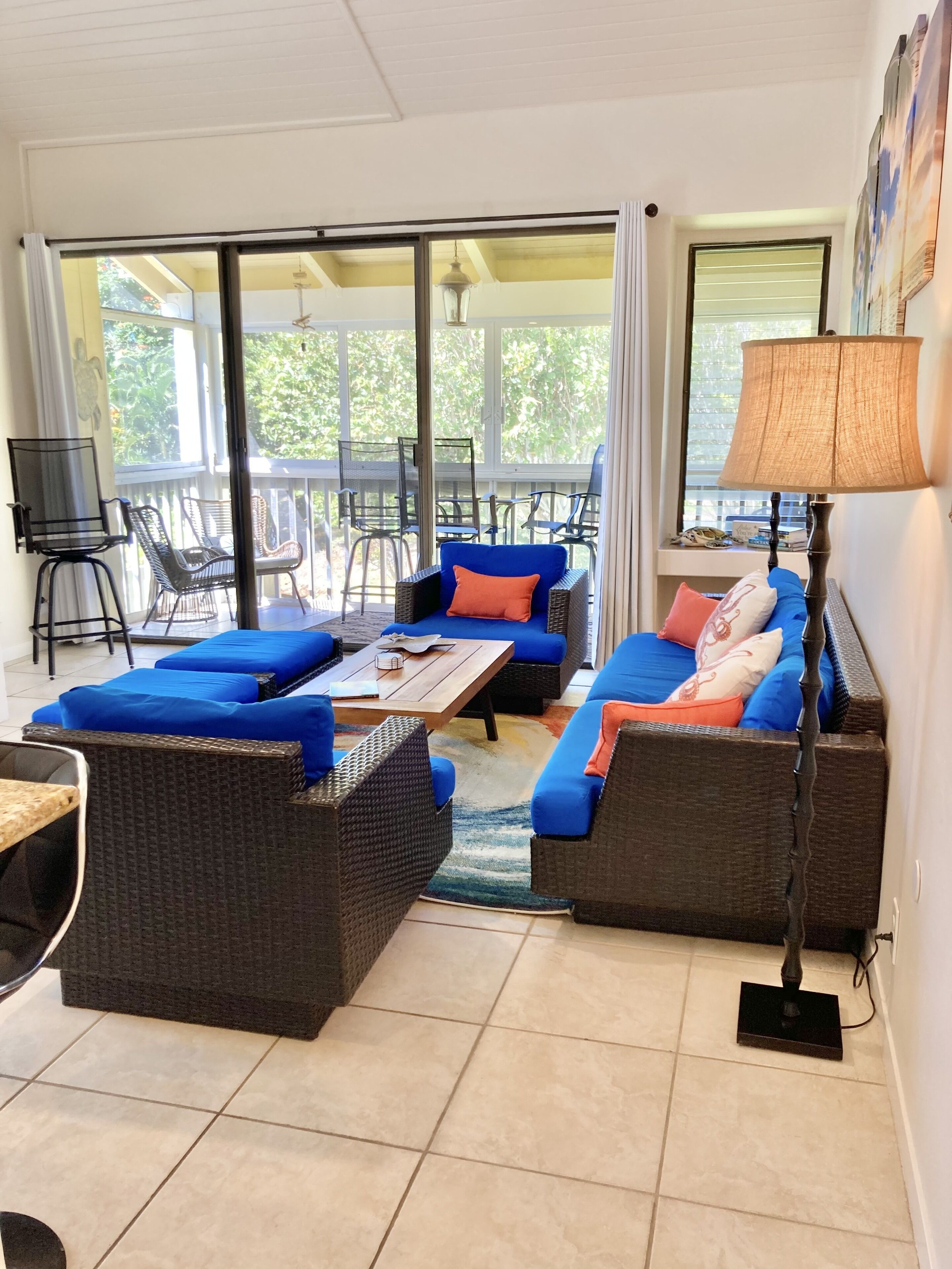 Amplia sala de estar con un ventanal grande, muebles de mimbre y una mesa.