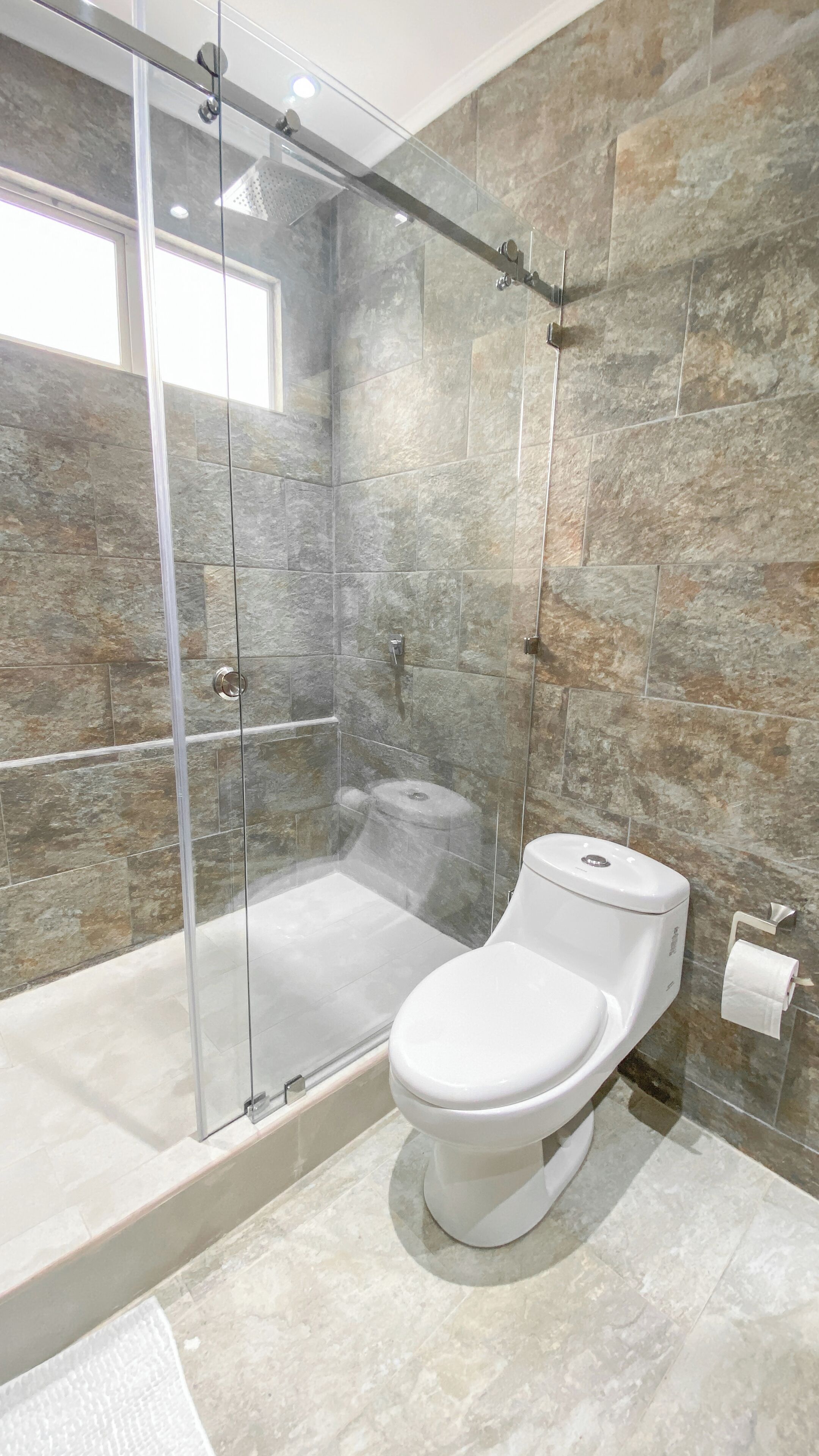 A modern bathroom with a glass-enclosed shower, a white toilet, and stone walls.