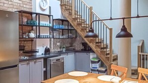 Una cocina con una escalera de madera, una mesa de comedor con individuales y un reloj en la pared.