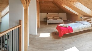 Un dormitorio con techo inclinado de madera, una cama con manta roja y una mesita de noche.
