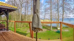 Una terraza de madera con un área de estar techada, vista a un lago y árboles circundantes.