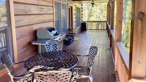 Un portico coperto con un tavolo rotondo e sedie, un barbecue e vista sulla foresta circostante.