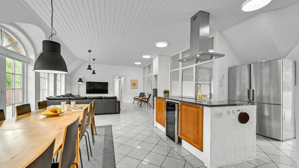 Une cuisine moderne dotée d’un îlot central, d’appareils électroménagers en acier inoxydable et d’un coin repas avec une table et des chaises en bois.