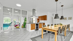 Une cuisine moderne avec des meubles en bois, un coin repas comprenant une table et des chaises en bois, et une grande fenêtre donnant sur une piscine.