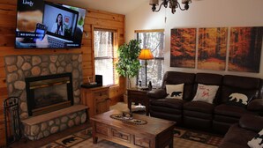 A cozy living room with a stone fireplace, a comfortable couch, and a television mounted on the wall. - Relaxing 3 bedroom retreat in the pines , come relax in tranquility,<br>  (Pinetop)