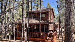 A rustic cabin surrounded by tall trees, featuring a wooden deck and a porch. - Relaxing 3 bedroom retreat in the pines , come relax in tranquility,<br>  (Pinetop)