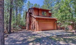 A rustic wooden cabin with a garage, surrounded by a forest.