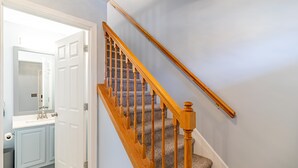 A staircase with wooden balusters and carpeted steps leading to a room with a white door and a bathroom with a blue vanity. - Seaside Park 3BR Beach Home – Family-Friendly, Walk to Beach + Peloton + Badges (Seaside Park)