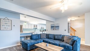 A modern living room with a sectional sofa, a wooden coffee table, and a view of the kitchen and dining area. - Seaside Park 3BR Beach Home – Family-Friendly, Walk to Beach + Peloton + Badges (Seaside Park)