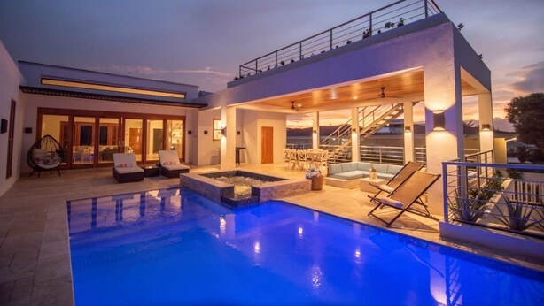 Ein modernes Haus mit Swimmingpool, Sitzgelegenheiten im Freien und einer Treppe, die zu einer zweiten Etage führt.