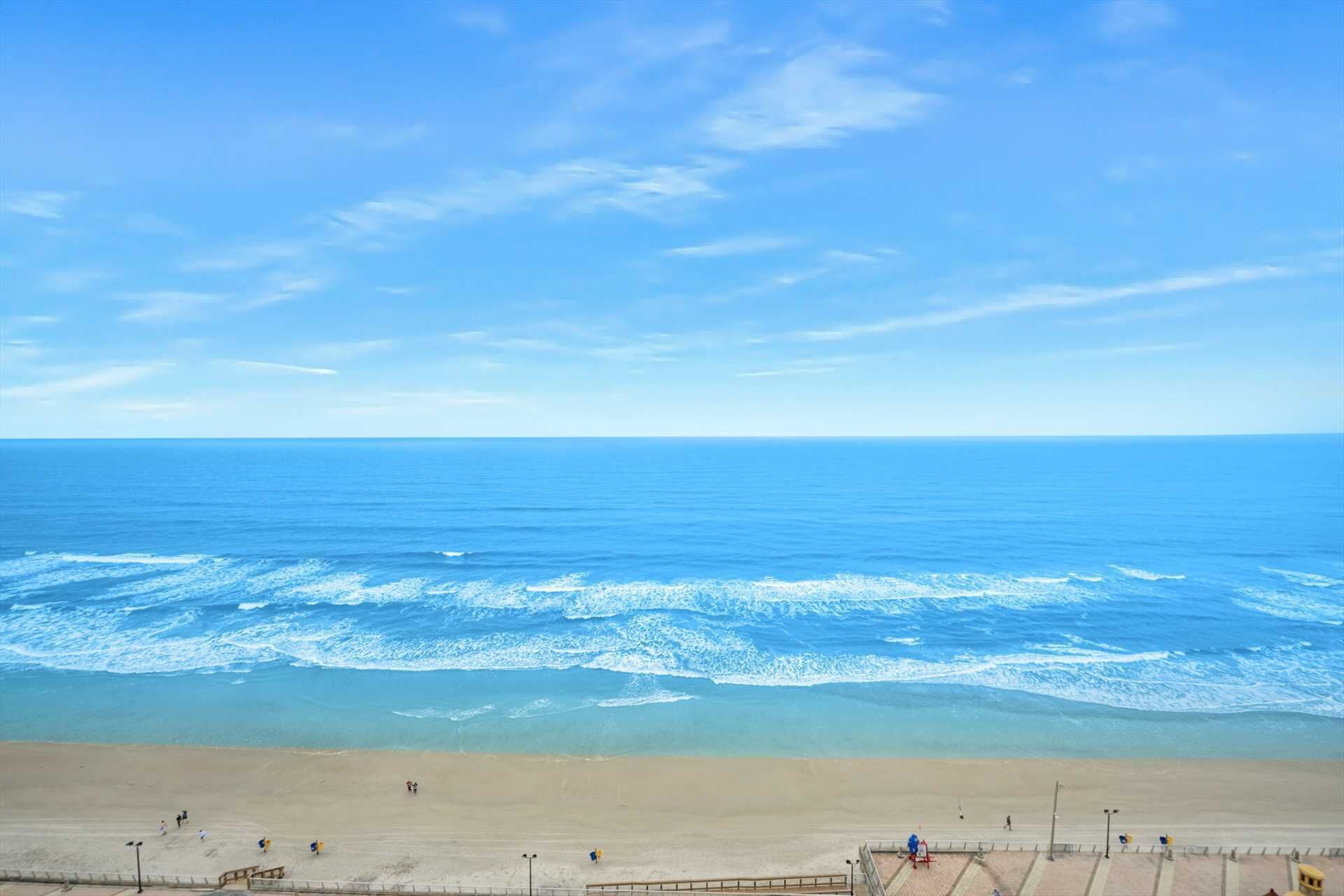 A beach with a clear sky, waves, and a few people.