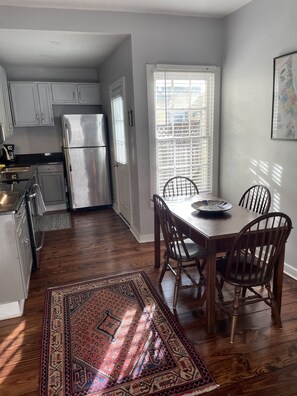 Cocina compacta con refrigerador, alacenas y una mesa de comedor con sillas.