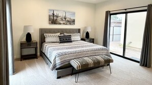 Ein Schlafzimmer mit einem Bett, zwei Nachttischen, einem Deckenventilator, einem Fenster mit Vorhängen und einem Wandbild mit Wüstenthema.