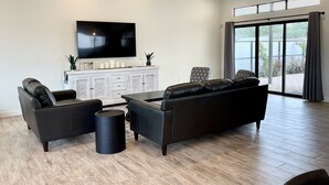 Ein modernes Wohnzimmer mit großem Flachbildfernseher, zwei Ledersofas, einem Couchtisch und einem weißen Schrank.