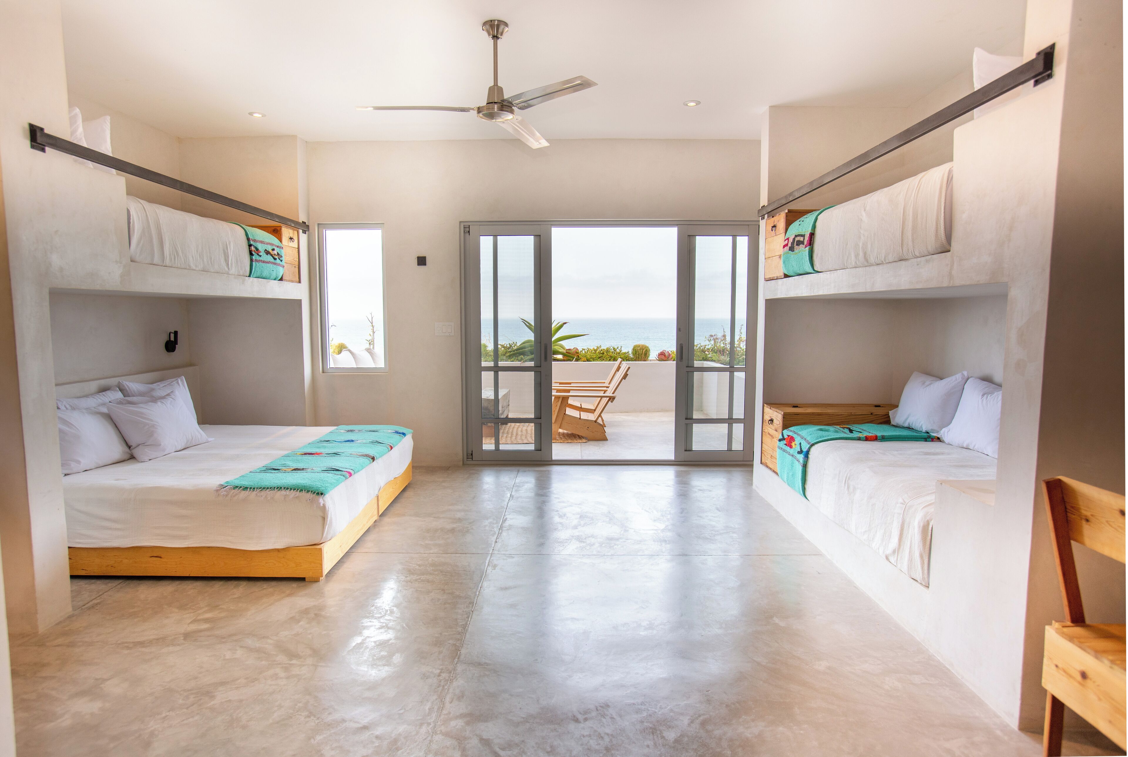 A room with two bunk beds, a ceiling fan, and a view of the ocean through large sliding doors.