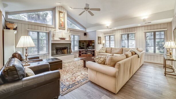 A spacious living room with a fireplace, large windows, and a ceiling fan. - Charming Sea Pines Retreat – 4th Row from the Beach with EV Charger (Hilton Head Island)