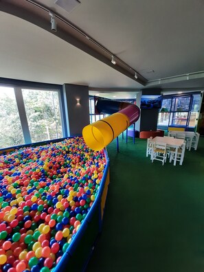 A ball pit with a slide, tables, and chairs in a room with large windows. - Hotel (Gramado)