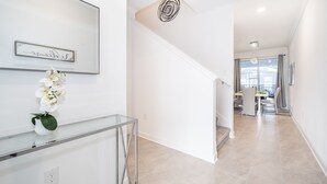 Ein modernes Interieur mit einer Treppe zu einem Essbereich, einem weißen Konsolentisch mit einer Vase weißer Blumen und einem an der Wand befestigten abstrakten Kunstwerk.