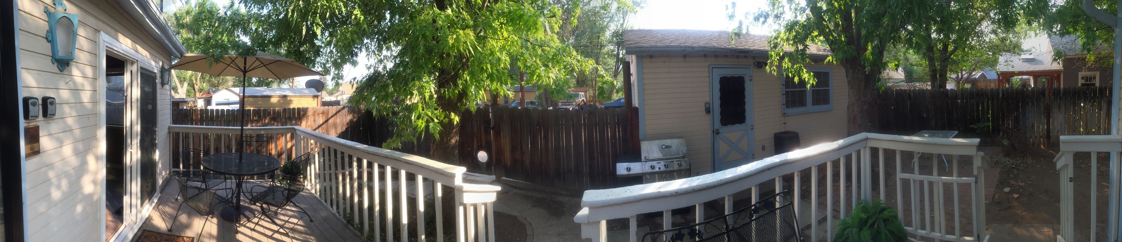 Eine Terrasse mit Tisch und Stühlen, ein Grill und ein kleines Gartenhaus.