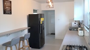 Une cuisine moderne avec un réfrigérateur noir, une cuisinière à gaz, des tabourets de bar en bois et un luminaire suspendu.
