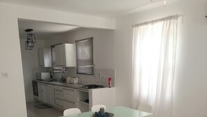 Une cuisine moderne avec des meubles blancs, une cuisinière à gaz et un coin repas comprenant une table en verre et des chaises blanches.