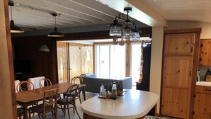 A kitchen with wooden cabinets, a dining table with chairs, a bar area, and a window with curtains. - Rustic-chic cottage with fantastic lake access, 15 minutes to Ithaca (Ithaca)