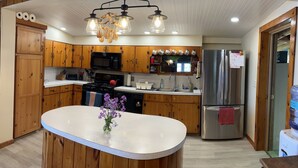 A kitchen with wooden cabinets, a central island, a stainless steel refrigerator, and a hanging light fixture. - Rustic-chic cottage with fantastic lake access, 15 minutes to Ithaca (Ithaca)